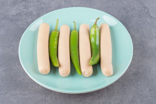 A blue plate of boiled sausages with chili peppers