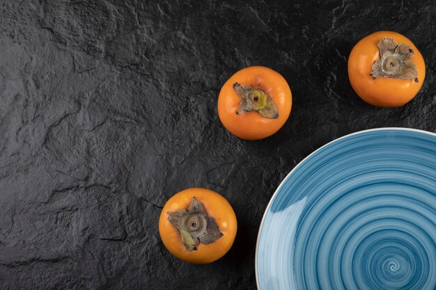 Синяя тарелка вкусной спелой хурмы фую на черной поверхности