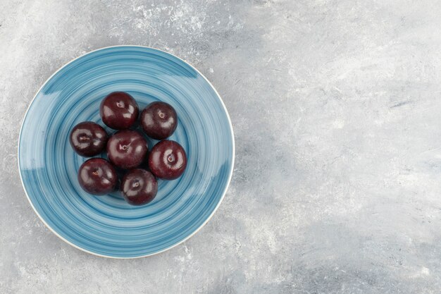 Blue plate of fresh purple plums on marble surface.