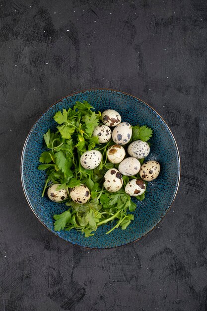 Blue plate of fresh raw quail eggs and parsley leaves on black surface.