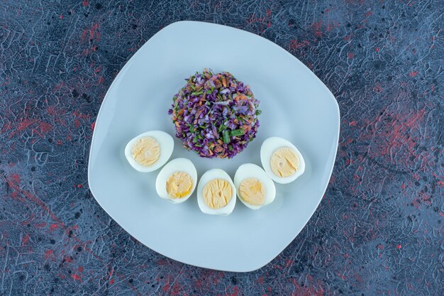 Голубая тарелка сваренных вкрутую яиц с овощами.