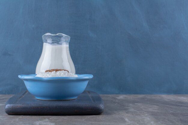 Голубая тарелка здоровой овсяной каши со стеклянной банкой молока на деревянной доске.