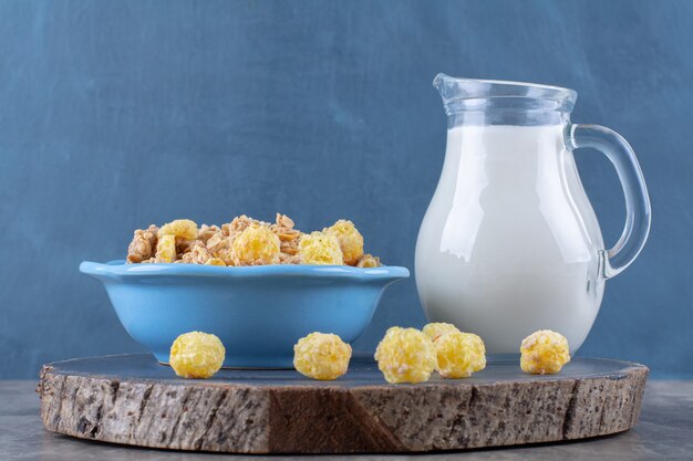 A blue plate of healthy sweet cornflakes with a glass jar of milk on a wooden piece . 