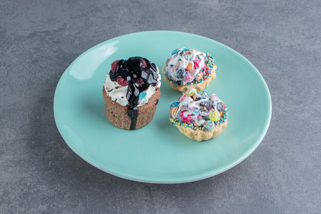 A blue plate of three sweet cupcakes with sprinkles