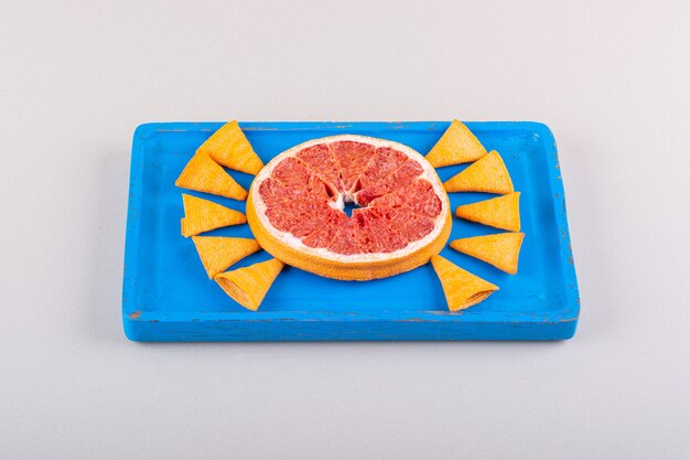 Blue plate of triangle chips and grapefruit slice on white background. High quality photo