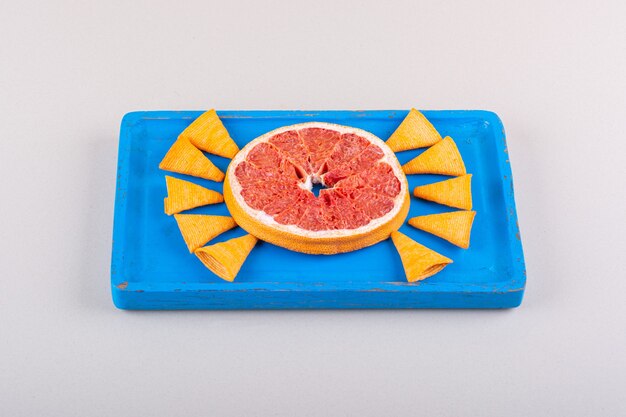 Синяя тарелка треугольных чипсов и ломтик грейпфрута на белом фоне. Фото высокого качества