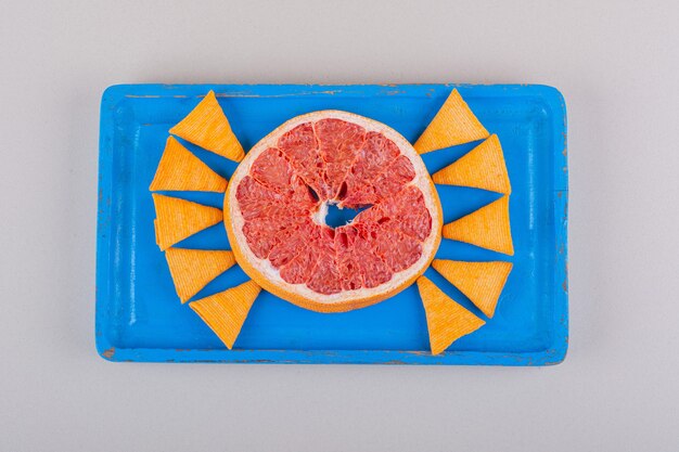 Blue plate of triangle chips and grapefruit slice on white background. High quality photo