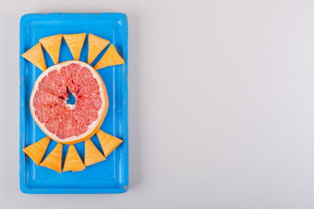 Blue plate of triangle chips and grapefruit slice on white background. High quality photo