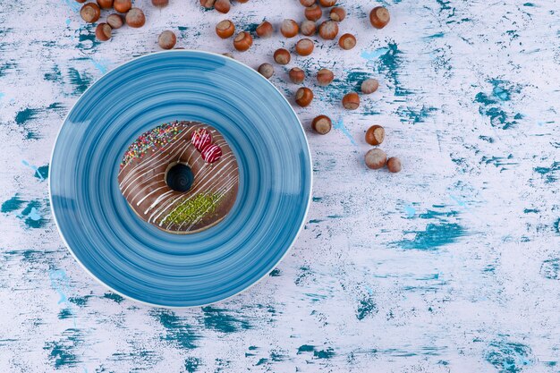 Голубая тарелка с шоколадным пончиком и очищенными фундуками на белой поверхности.