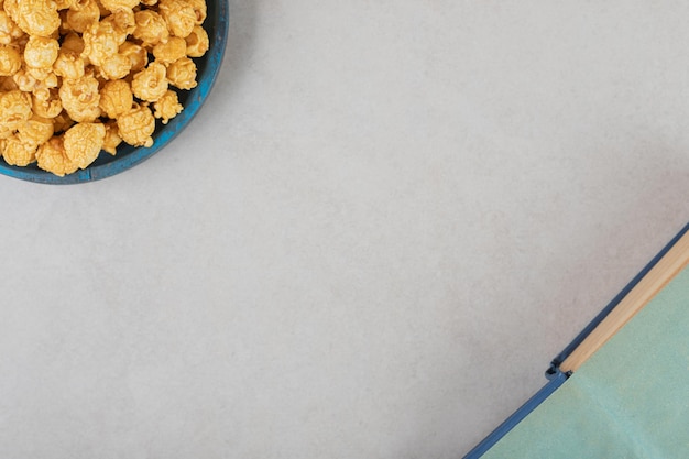 Blue platter filled with caramal coated popcorn next to an open book on marble background.