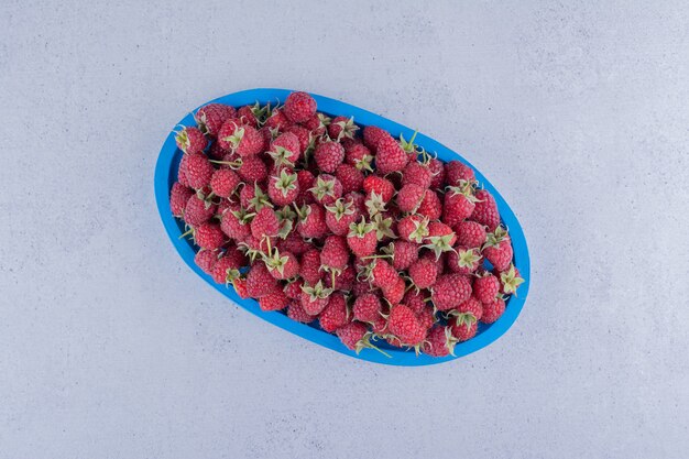 Blue platter with a serving of fresh raspberries on marble background.