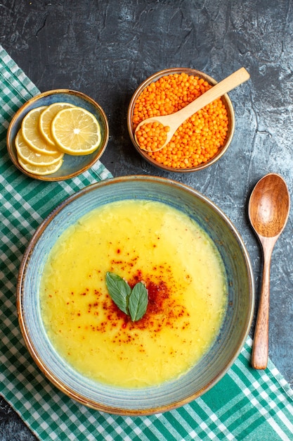 A blue pot with tasty soup served with mint and pepper next to chopped lemon wooden spoon and yellow pea on blue background