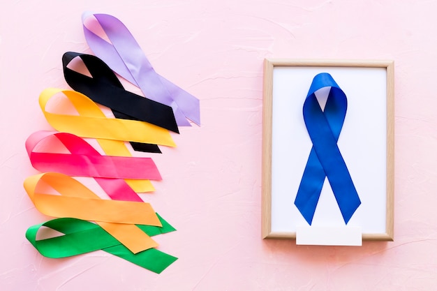 Blue ribbon on white wooden frame near the row of colorful awareness ribbon