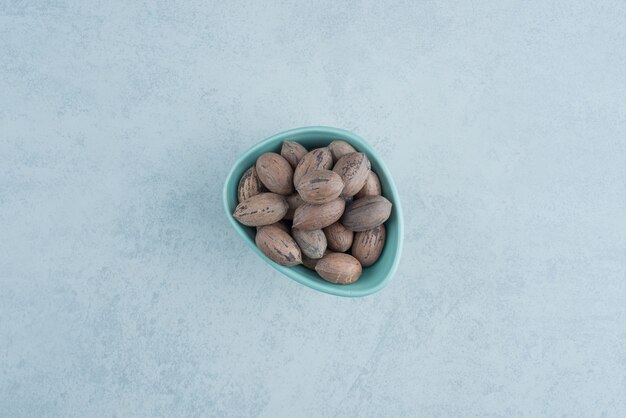 Голубая тарелка, полная орехов на мраморном фоне. Фото высокого качества