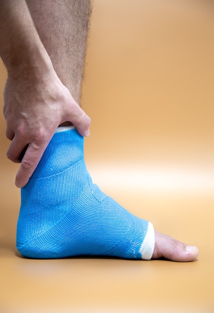 青い添え木足首。色付きのぼやけた背景の男性患者に包帯を巻いた脚。スポーツ傷害の概念。