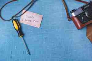 Free photo blue surface with camera, screwdriver and note for father's day