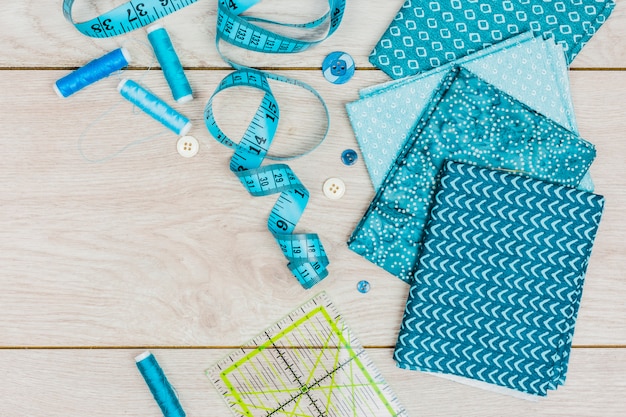 青い糸。巻き尺;ボタン定規と折られたプリント服を木製の机の上