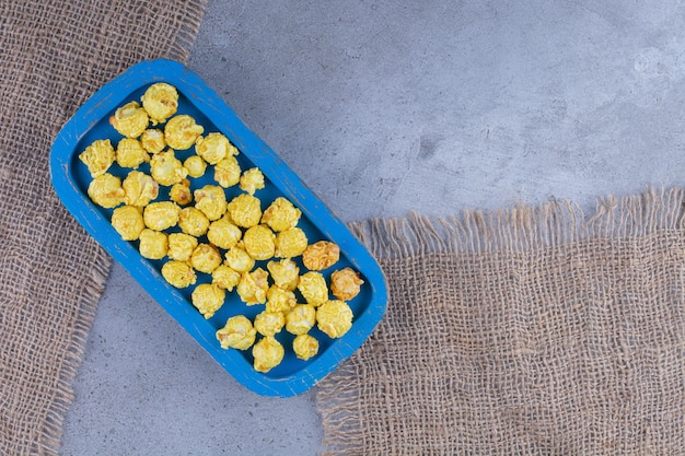 Foto gratuita vassoio blu con una manciata di caramelle popcorn gialle su pezzi di stoffa su una superficie di marmo