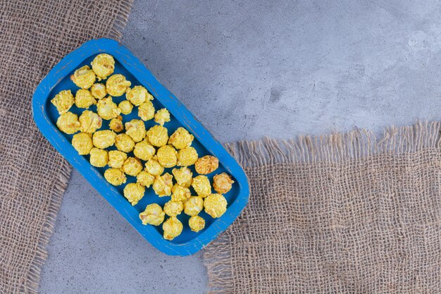 Blue tray with a handful of yellow popcorn candy on pieces of cloth on marble surface