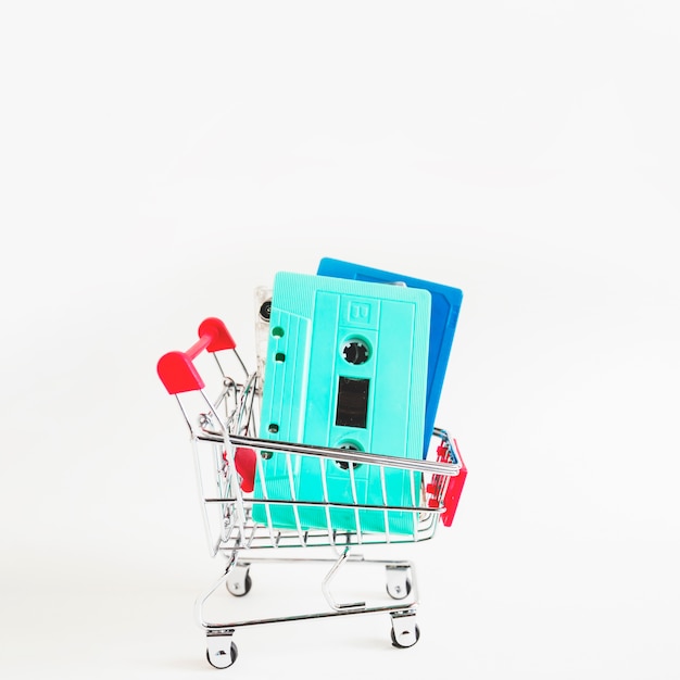 Blue and turquoise cassette tapes in shopping cart isolated over white background