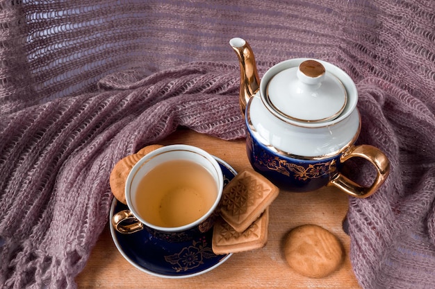 Blue-white kettle with a cup and saucer on an old wooden table with cookies.