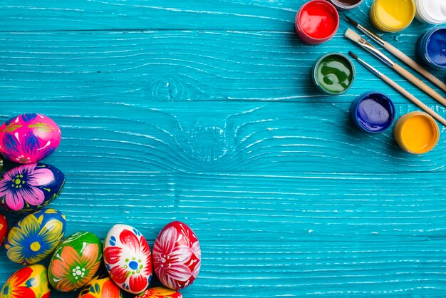 Синий деревянный фон с пасхальными яйцами и краской банок