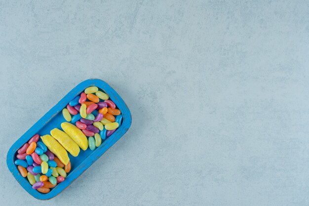 A blue wooden board of banana shaped chewing candies with colorful beans candies