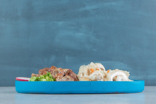 A blue wooden board of chicken meat with vegetable salad.