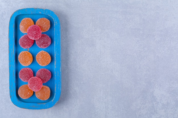 A blue wooden board full of red and orange sugary marmalades . 