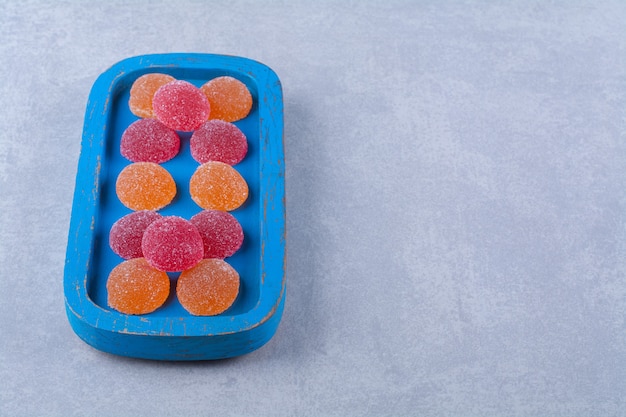 A blue wooden board full of red and orange sugary marmalades 