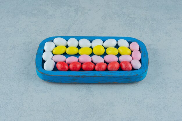 A blue wooden board full of round sweet colorful candies on white surface