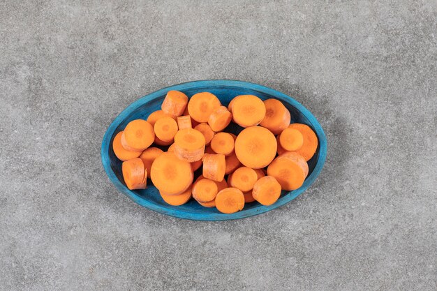 A blue wooden board full of sliced carrots placed on a stone surface.