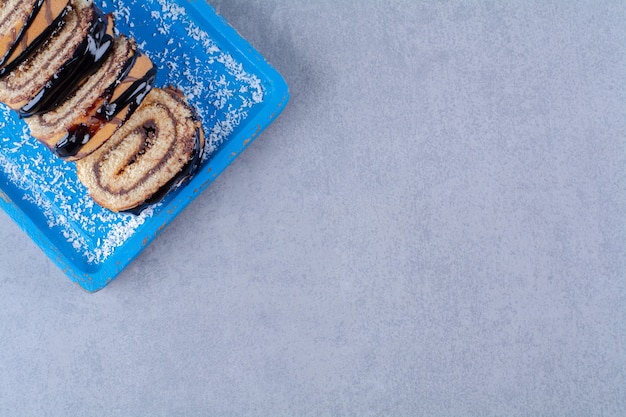 Синяя деревянная доска нарезанного сладкого рулета с шоколадным сиропом.