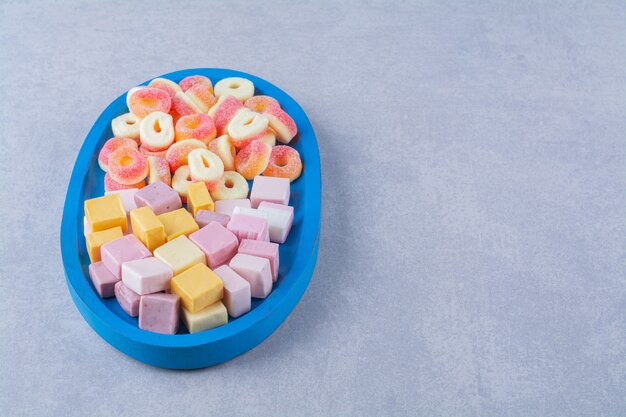 A blue wooden board of sugary red jelly candies with sweet rainbow liquorice . 