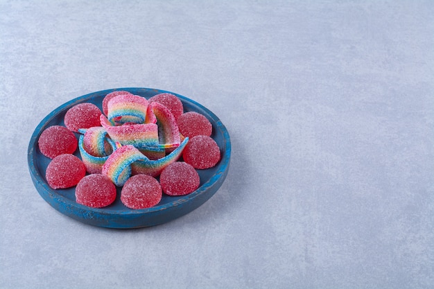 A blue wooden board of sugary red jelly candies with sweet rainbow liquorice . 