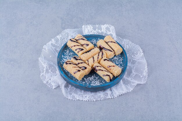 A blue wooden board of sweet sticks with sprinkles and chocolate syrup . 