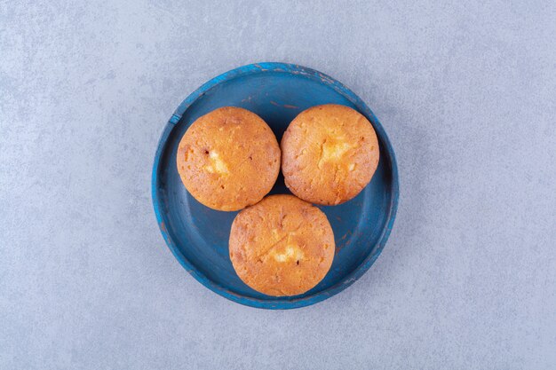 A blue wooden board of three sweet fresh cupcakes . 