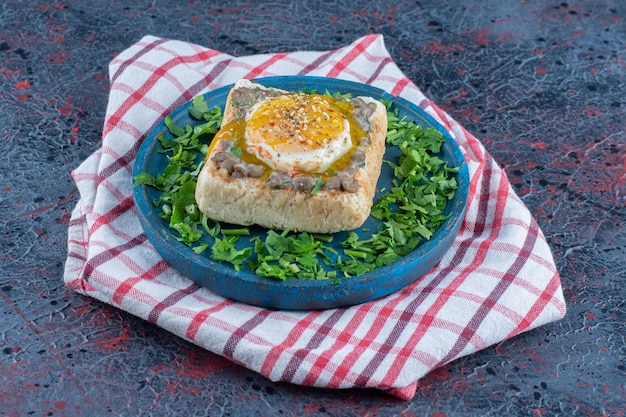 Un tagliere di pane tostato in legno blu con uovo ed erbe aromatiche