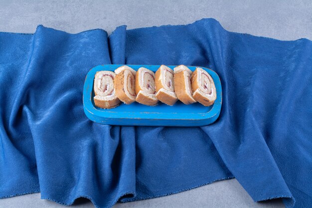 A blue wooden board with sweet sliced rolls on tablecloth . 