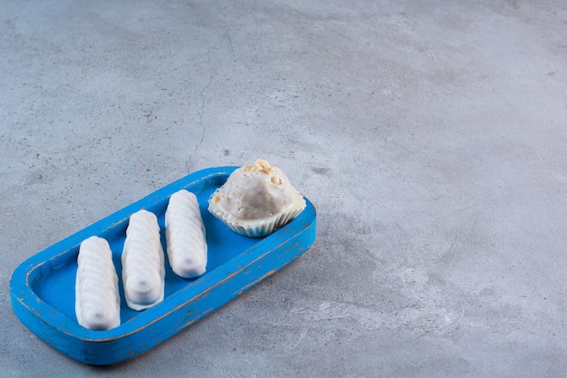 A blue wooden board with sweet white sticks and cupcake.