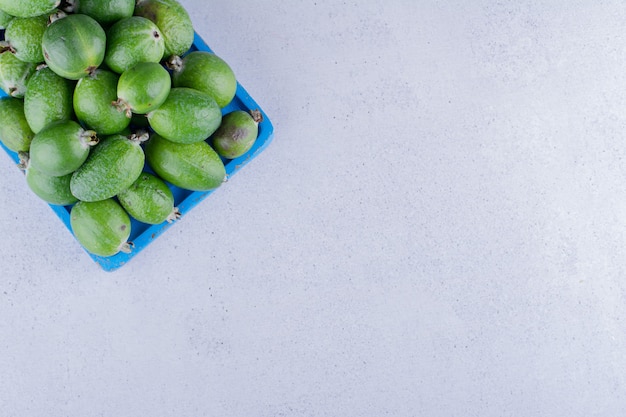 Blue wooden platter stocked with a heap of feijoas on marble background. High quality photo
