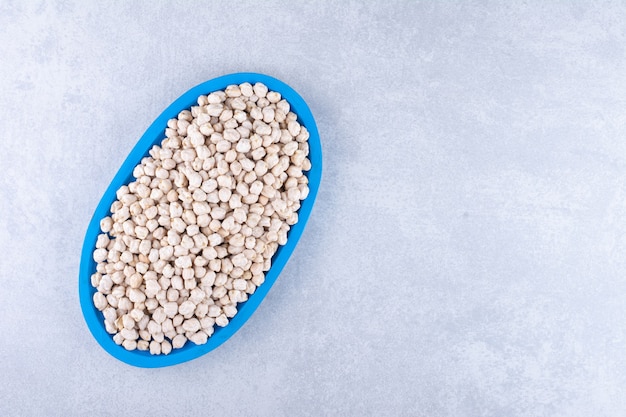 Free photo blue wooden platter stocked with raw chickpeas on marble surface