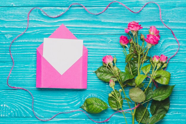 Blue wooden surface with blank note on envelope and purple flowers