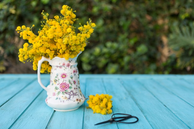 Blue wooden surface with vase, flowers and scissors