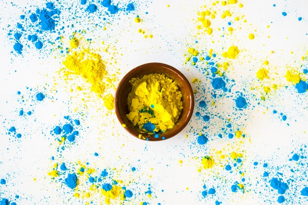 Blue and yellow color powder around the bowl on white backdrop