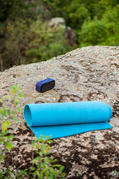 Blue yoga mat, wireless portable speaker on rock in canyon