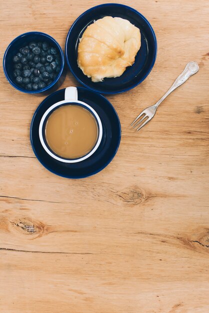 Blueberries bowl; bread and coffee with fork on wooden textured background