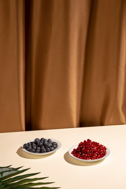 Blueberries and pomegranate seeds on plate with palm leaf over table against brown curtain