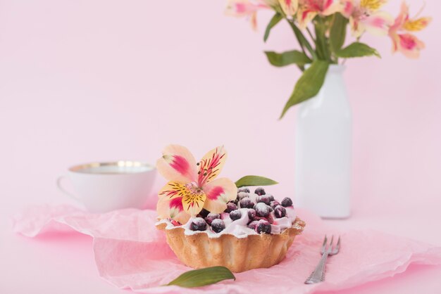 ピンクの背景に対してアルストロメリアの花で飾られたブルーベリーのタルト