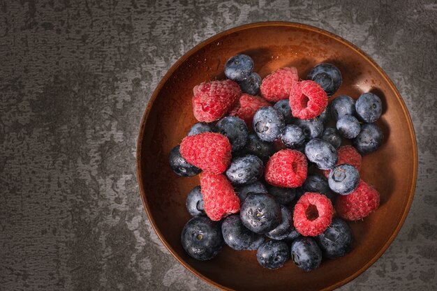 Blueberry and raspberry in a clay plate. Raw berries mix close up. Summer fresh berries.